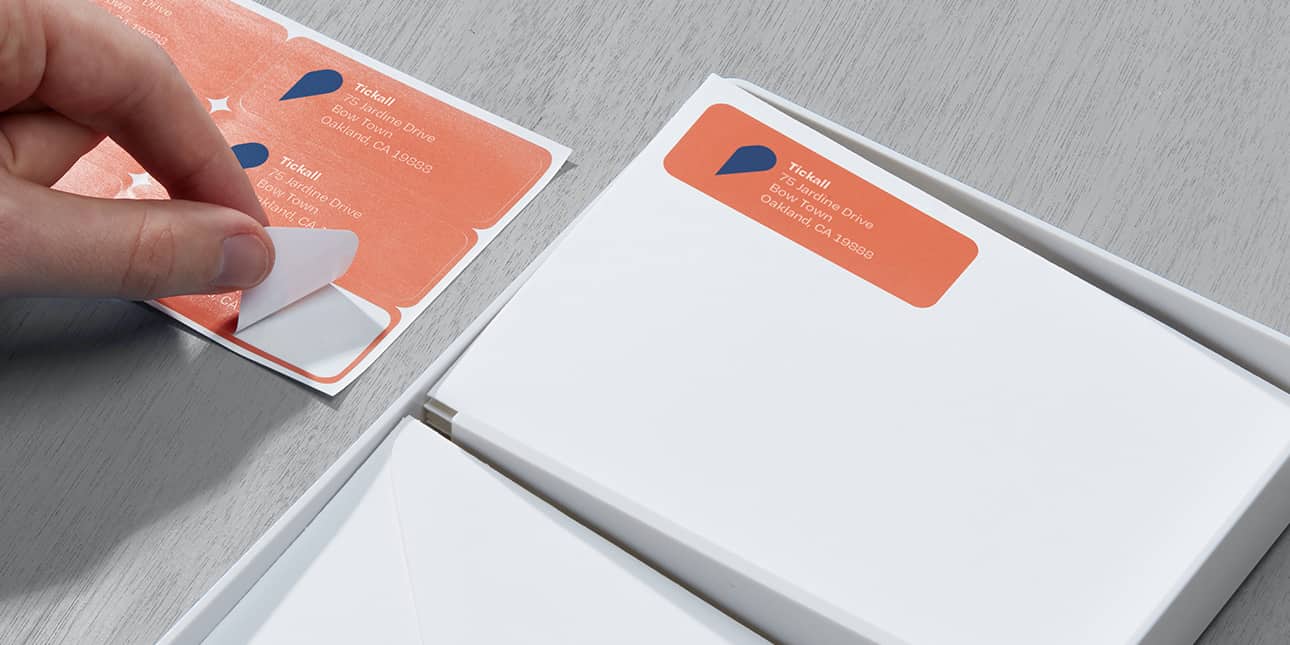 Orange mailing label on white envelope and hand removing a personalized return address label from a sheet of 9 address stickers