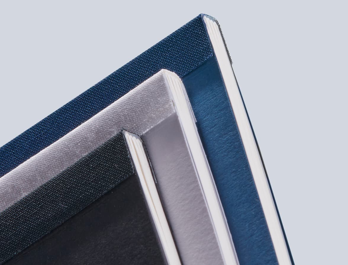 A close up image of the binding of three tape bound notebooks, varying in colour, placed on top of each other.