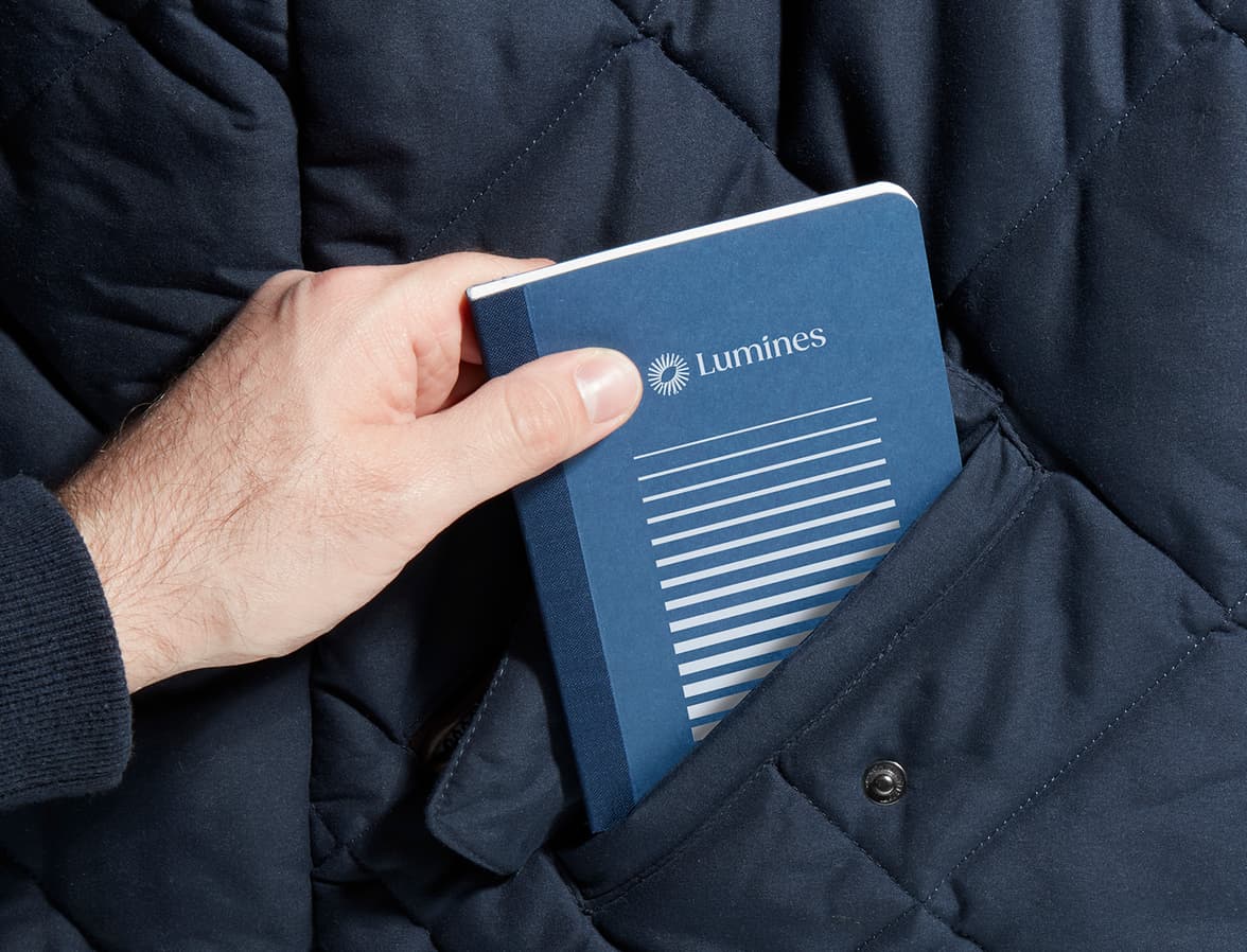 A hand placing a customised blue tape bound notebook into a jacket pocket.