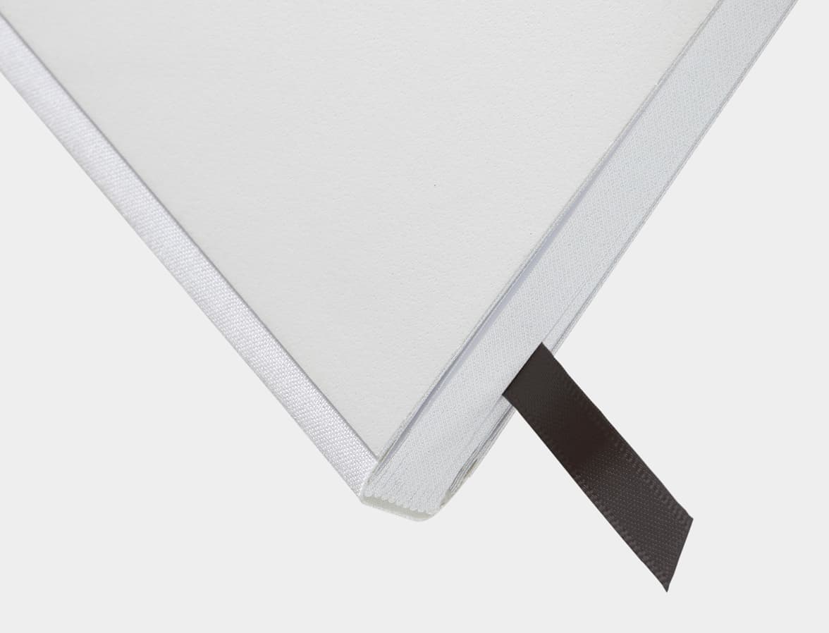 A close up of the bottom corner of a cloudy grey softcover notebook with a ribbon bookmark.