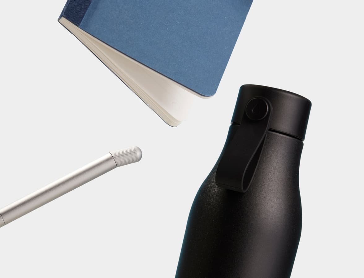 A collection of products including a tape bound notebook, pen and water bottle.