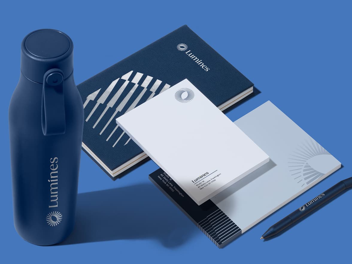 A collection of midnight blue and white branded merchandise products including notebooks, a pen and a water bottle with a blue background.