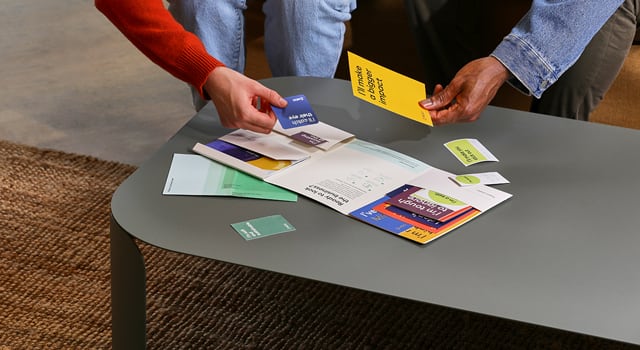 Hand holding a square Business Card from the MOO Sample Pack and various free printed product samples on a wooden drawer