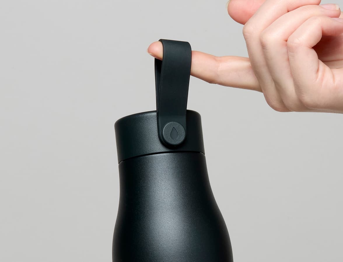 A close up of a person holding a jet black MOO water bottle by the top strap.