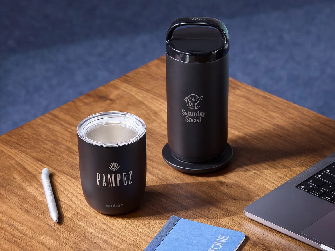 Two black customized tumblers placed on a wooden table alongside a aluminium pen.