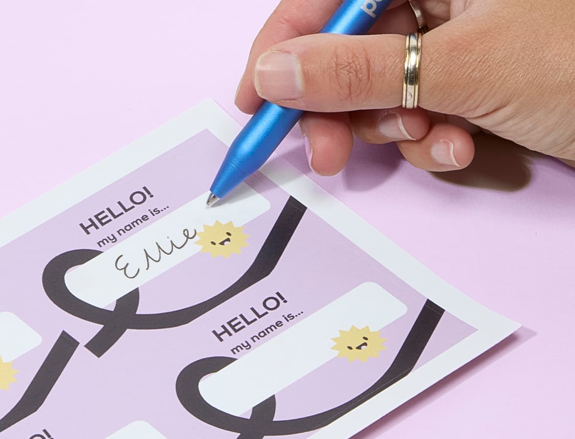 A close up of a hand writing on a customized lilac name tag.