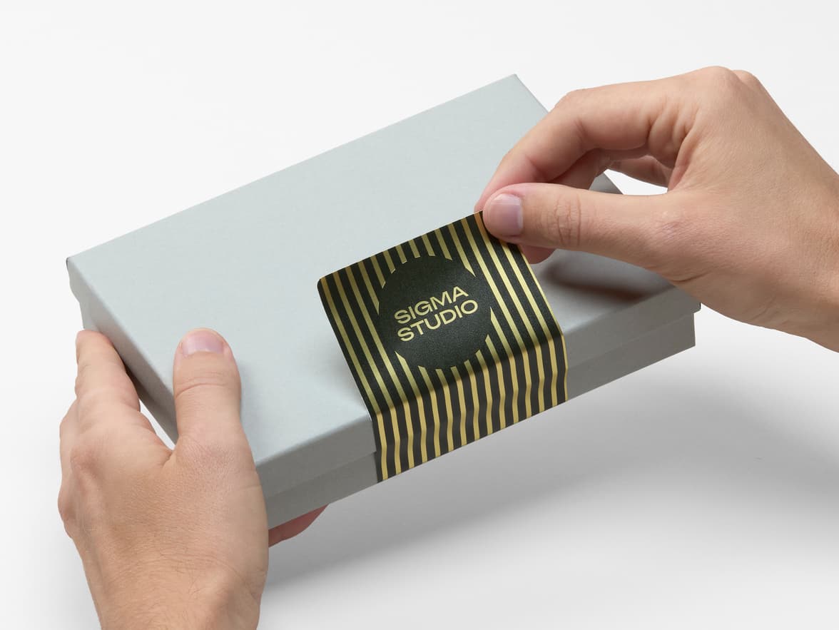 Hands placing a customized black and gold metallic sticker on a packaging box.