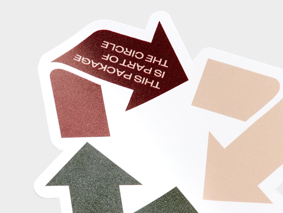 A close up image of a customized coated sticker in the shape of the recycling triangle.