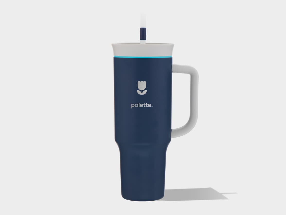 A navy blue tumbler with a white handle, white lid, and light blue accent ring, featuring a straw and the 'palette.' brand logo with a tulip icon.