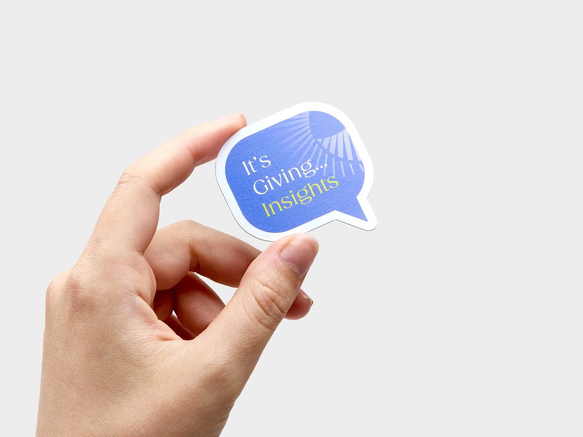 A hand holding a customized coated paper sticker in the shape of a speech bubble.