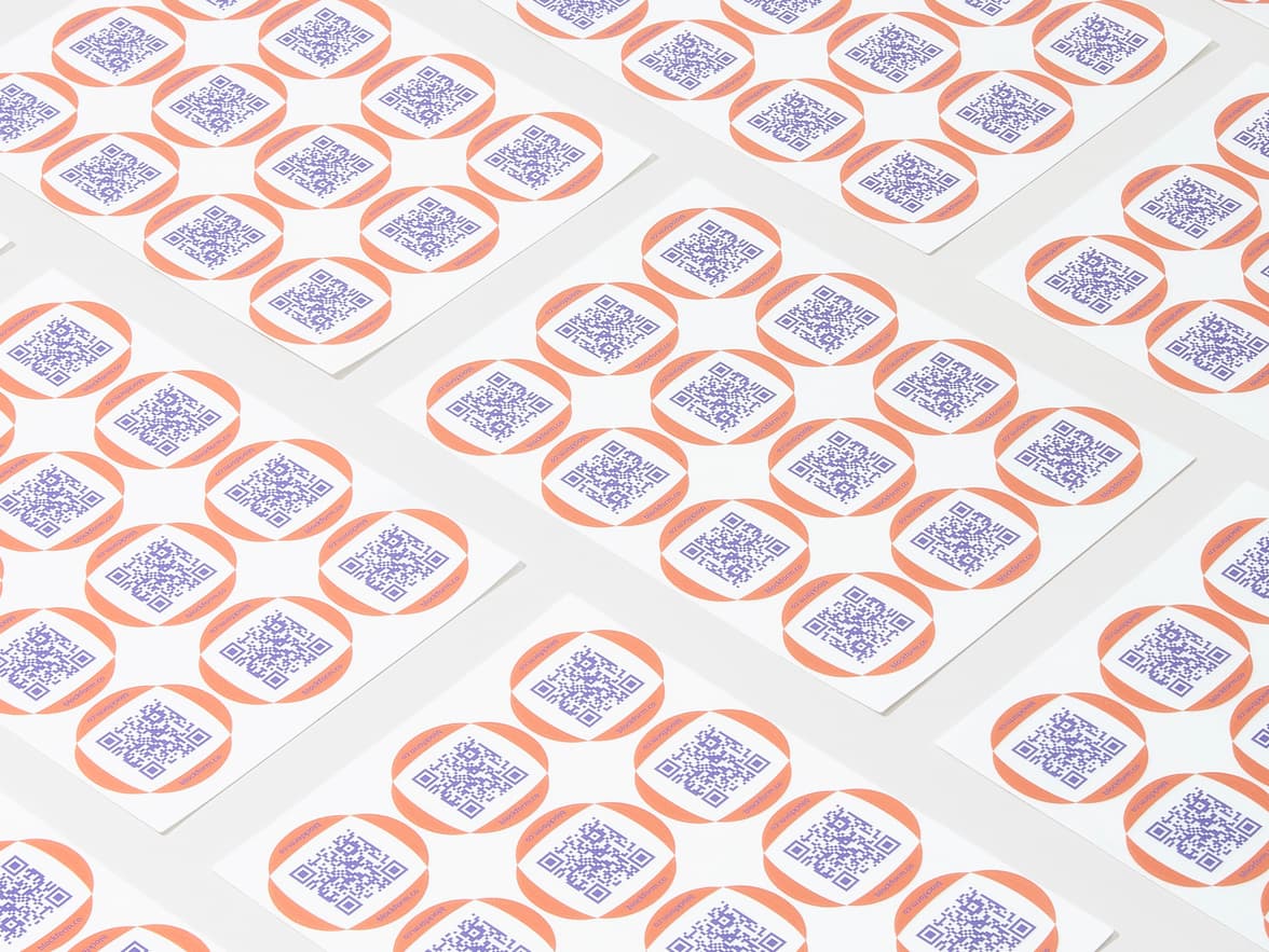 A collection of customized clear round stickers with purple QR codes printed on them.