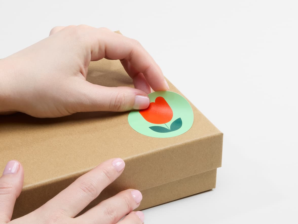 A person placing a customized plastic free matte paper sticker on a cardboard box.
