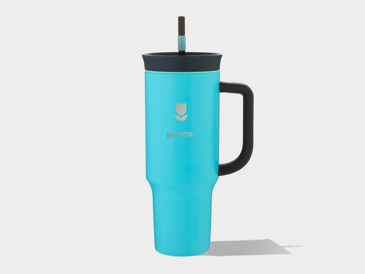 A turquoise palette. brand tumbler with a tulip logo, black handle, dark gray lid, and a straw.