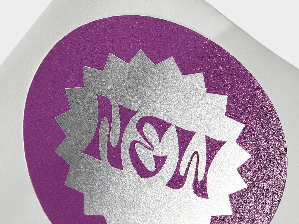 A close up image of a round silver sticker with purple customization.
