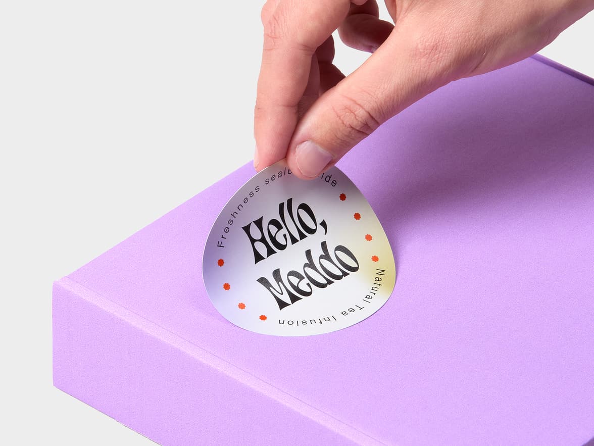 A hand placing a multi coloured customized round coated sticker onto a purple box.