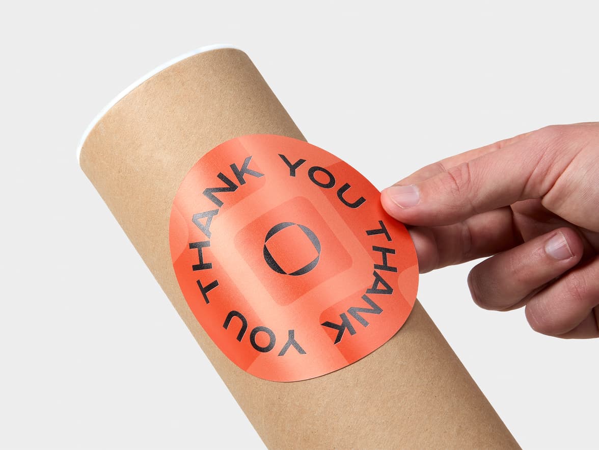 A hand placing a customized large round glossy paper stickers onto a round packaging tube.