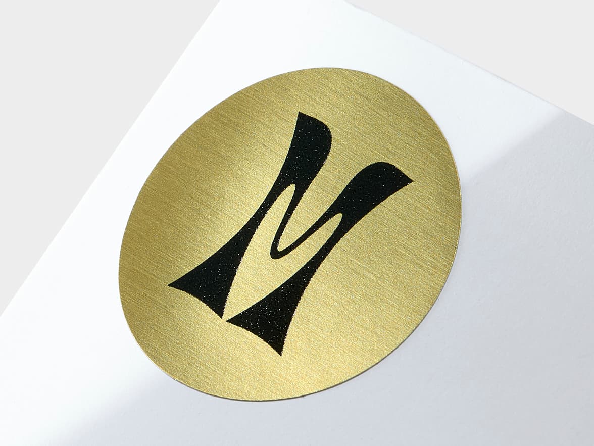 A close up image of a round gold custom metallic labels with black customization.