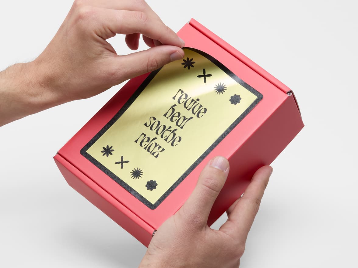 Hands placing a large gold metallic sticker on a red box.