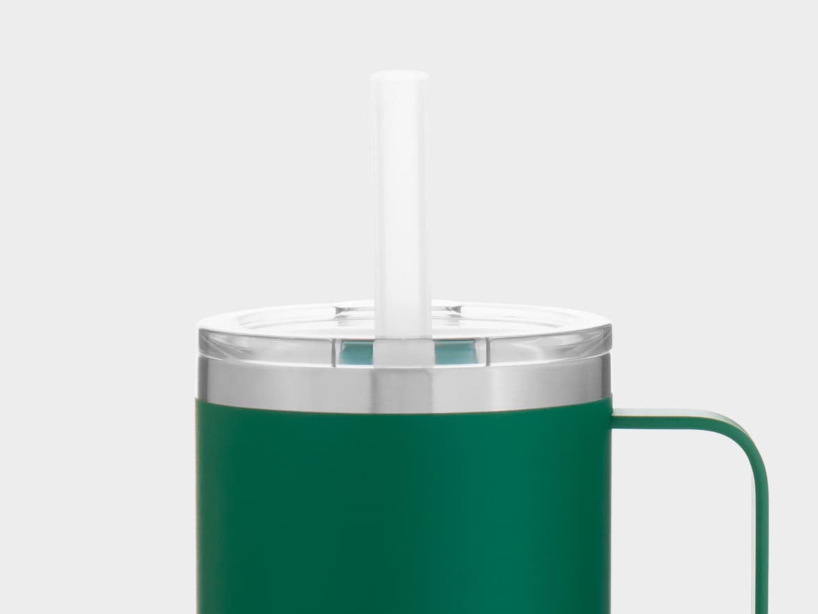 A close-up of a dark green insulated tumbler with a clear lid and a white straw. The tumbler has a silver-colored band around the top where the lid attaches and a matching green handle on the right side. The background is a solid light gray.