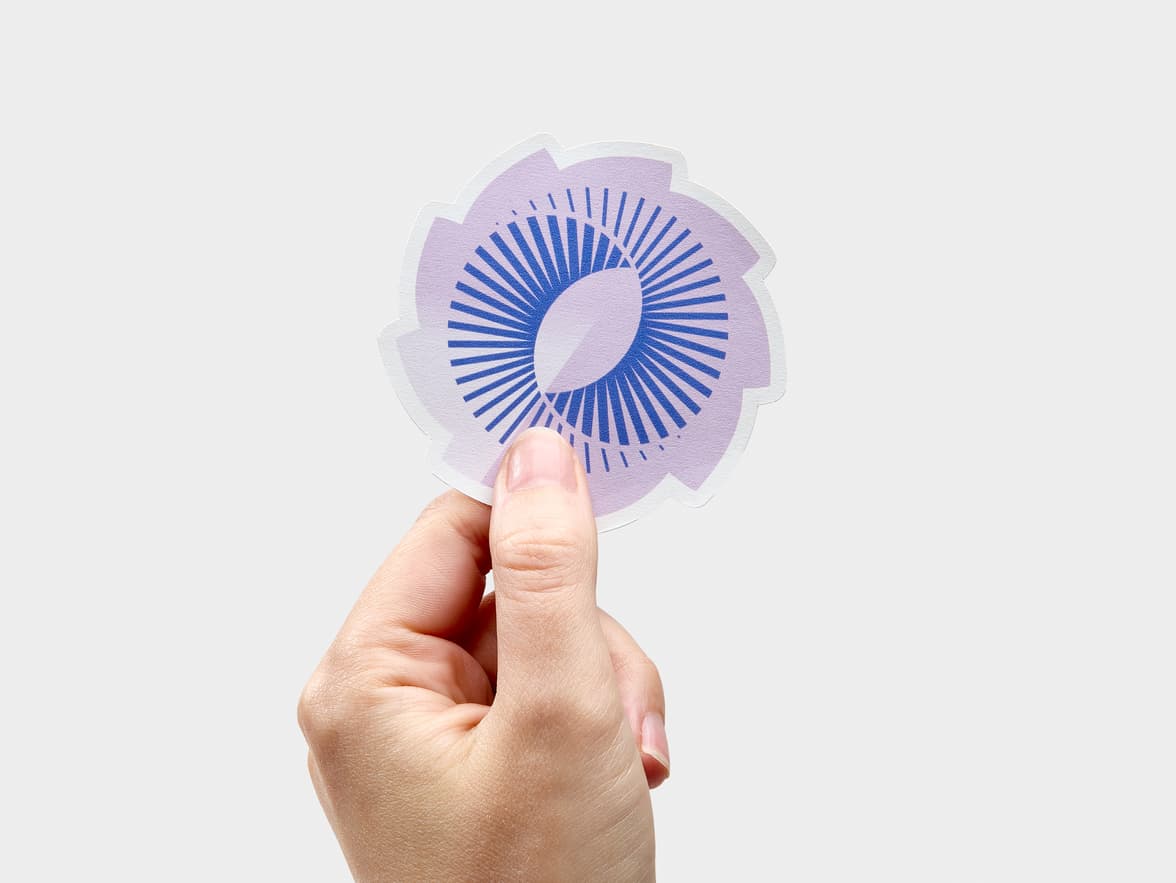 A hand holding a customized matte paper sticker in the design and shape of a spiral.
