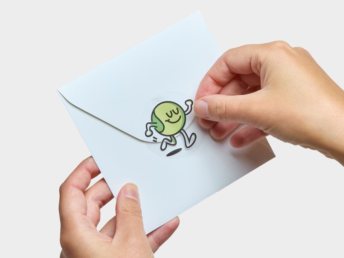 A hand placing a customized clear round sticker onto a white envelope.
