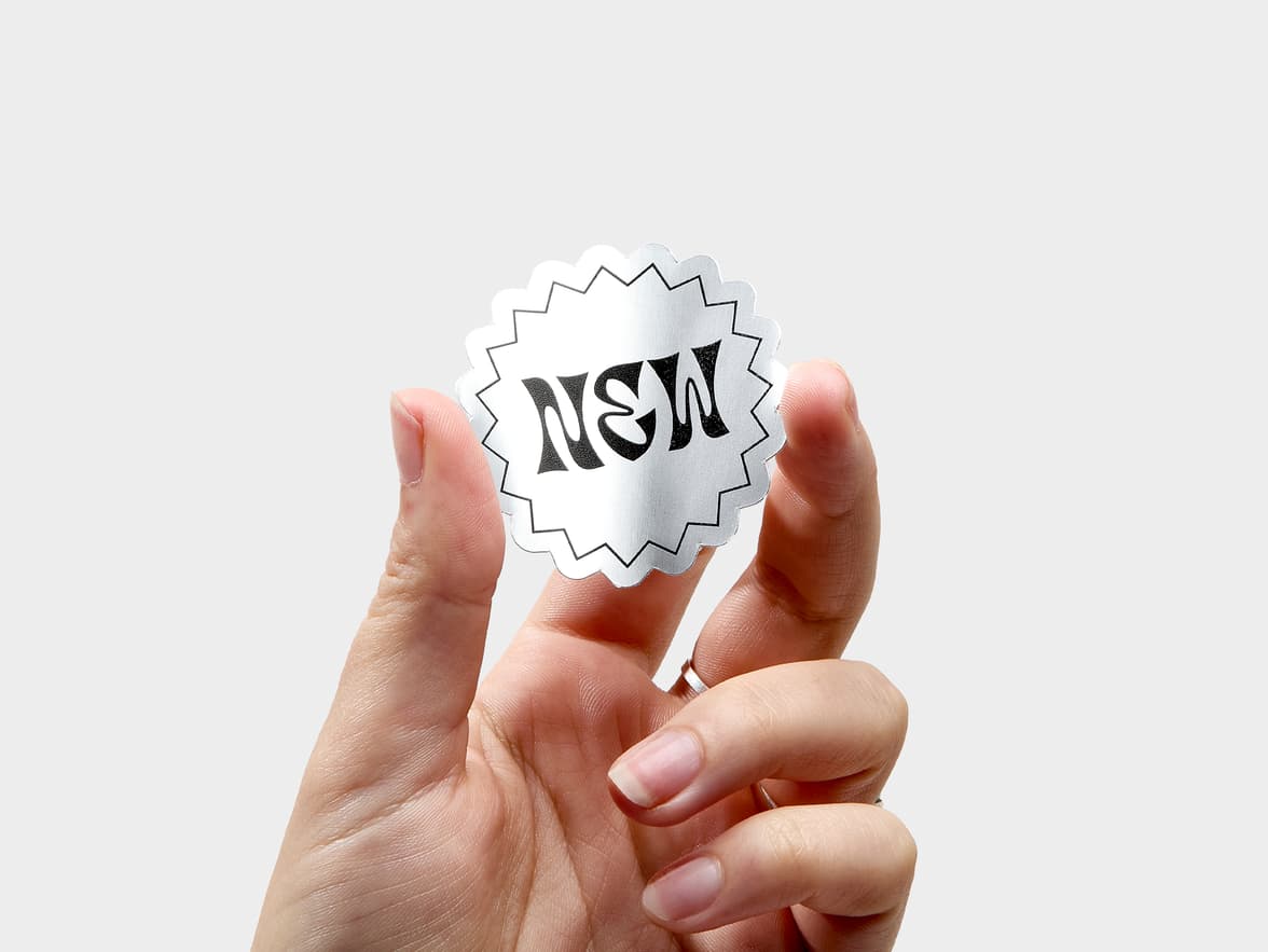 A hand holding a customized silver metallic sticker in the shape of a starburst.