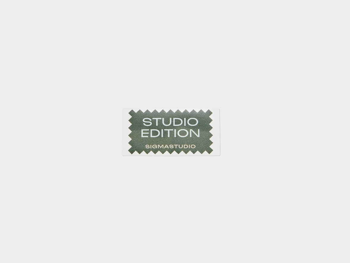 A white, rectangular sticker with serrated edges features a textured dark green center. White text on the center reads "STUDIO EDITION" and "SIGMASTUDIO" as branding.