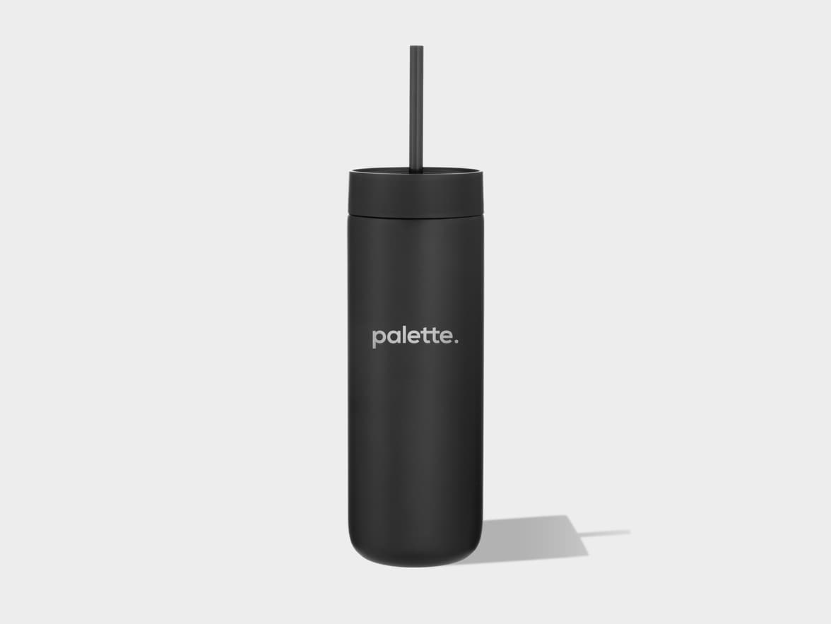 A black matte cylindrical tumbler with a lid and a straw, featuring the word "palette." in light gray on its side, casts a shadow on a light gray background.