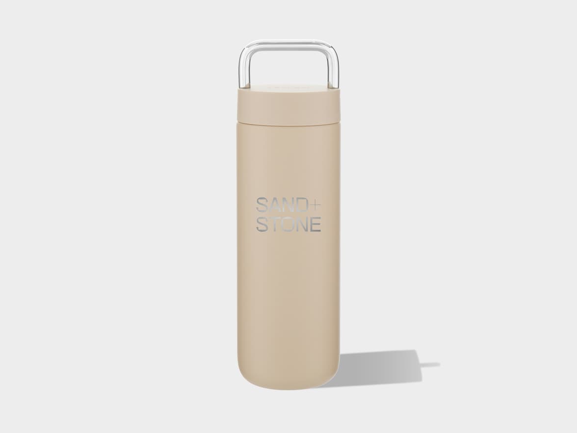 A beige tumbler with a clear handle and "SAND+ STONE" branding.