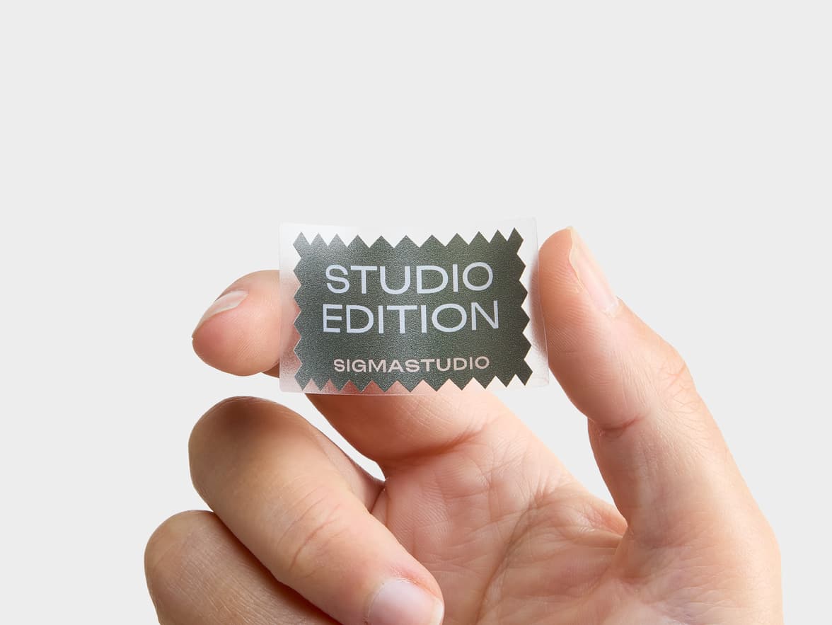 Clear, jagged-edged 'STUDIO EDITION SIGMASTUDIO' sticker held by a hand.