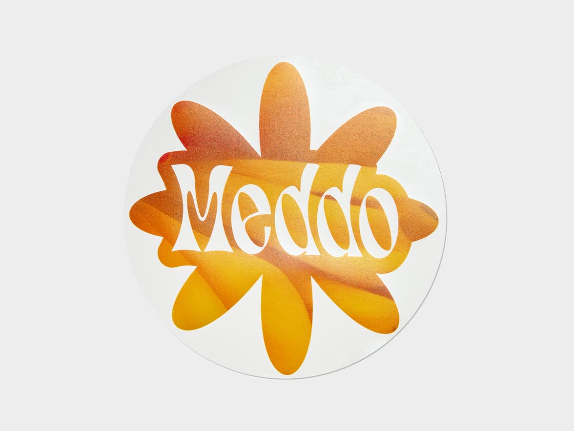A customized round clear sticker with an orange flower on it and the word 'Meddo'.