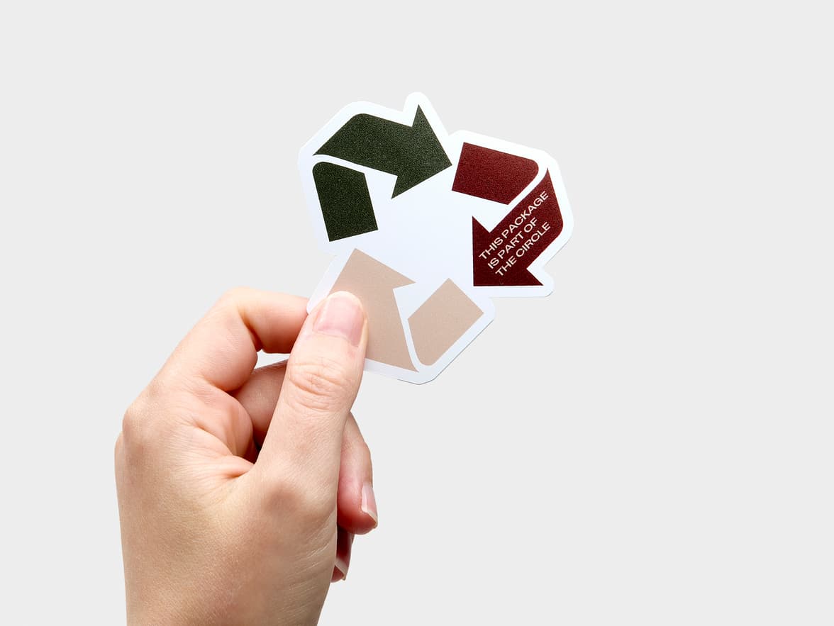 A hand holding a customized coated sticker in the shape of the recycling triangle.