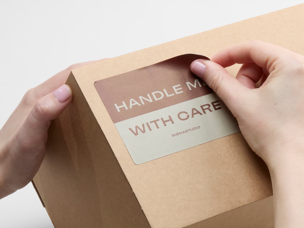A person placing a customized matte paper stickers for businesses in size 4x3 on a cardboard box 